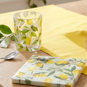 Mediterrane Tischdekoration mit gelbem Tischläufer, Zitronen-Servietten, Glas mit Zitronenmotiv, Windlicht und Kerze für sommerliches Wohnambiente.