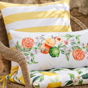 Sommerliche Terrassendekoration mit Rattan-Sessel, Zitronen-Sitzkissen, Zitrus-Kissen, Kerzen und Windlicht für mediterranes Dolce-Vita-Ambiente.